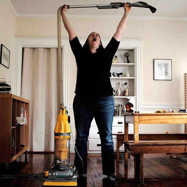 Femme qui tend en l'air le flexible de son aspirateur Dyson en signe de victoire